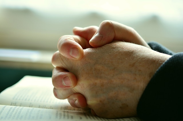 mains jointes en signe de prière devant une bible
